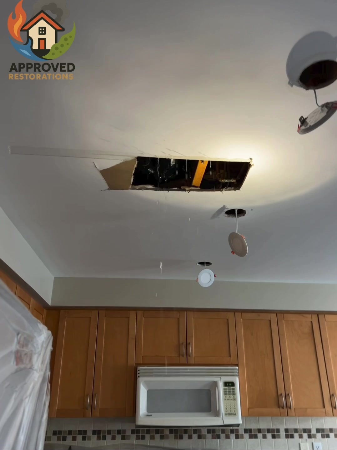 Water intrusion from an upstairs sewage backup is pouring through the kitchen ceiling, so our crew has already tarped the cabinets, dropped buckets under the still-dripping recessed lights, and is now cutting out the bulged drywall to contain and clean the contaminated water before it spreads further.