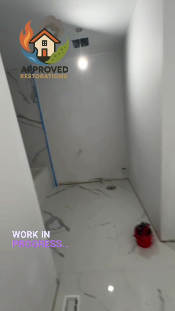 After tearing out the ruined materials from a severe water damage claim, our crew is deep into the reconstruction phase of this home bathroom, laying large marble-patterned floor tiles and wrapping the new bathtub surround in matching stone before we finish the fresh drywall and set the final fixtures.