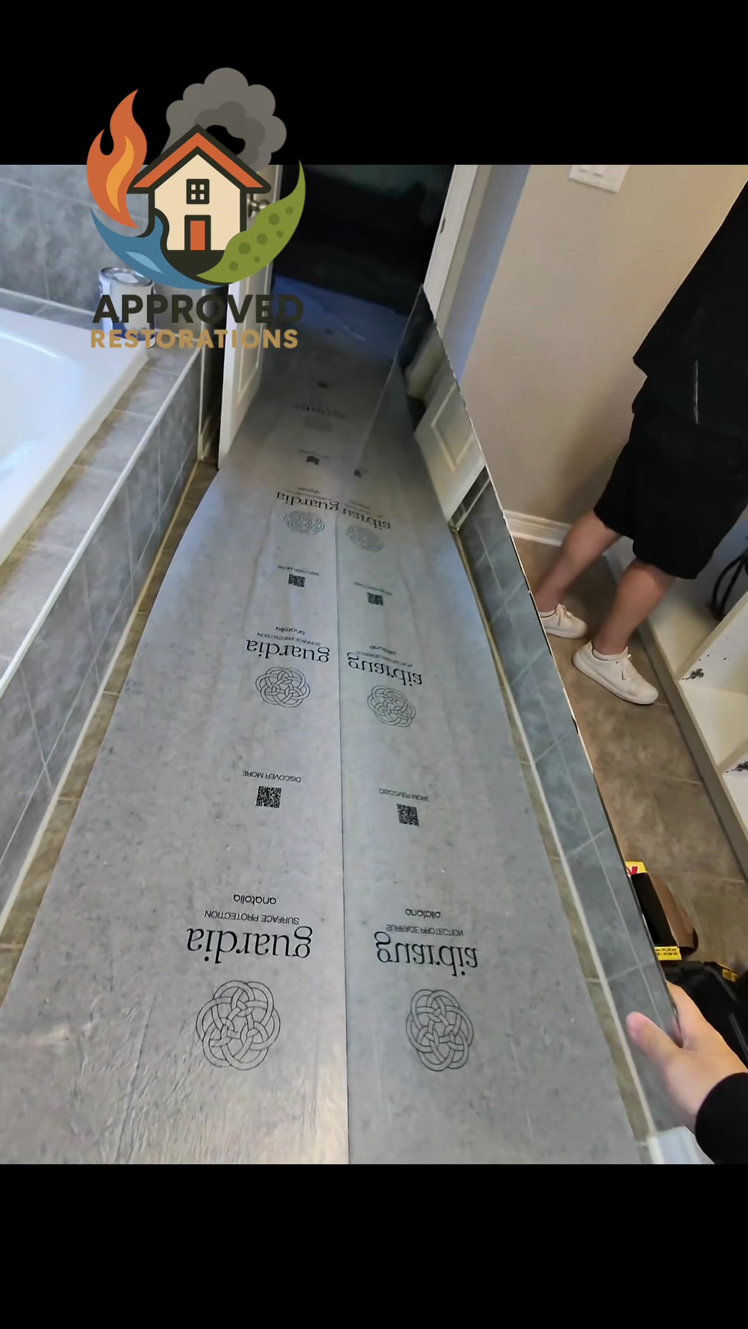 A hidden shower leak wrecked this bathroom floor and the ceiling below, so our crew is laying down heavy-duty surface protection and pulling the massive vanity mirror out of the work zone to inspect the saturated drywall, securing a clean pathway before we tear into the wet zones to map the damage for the insurance claim.