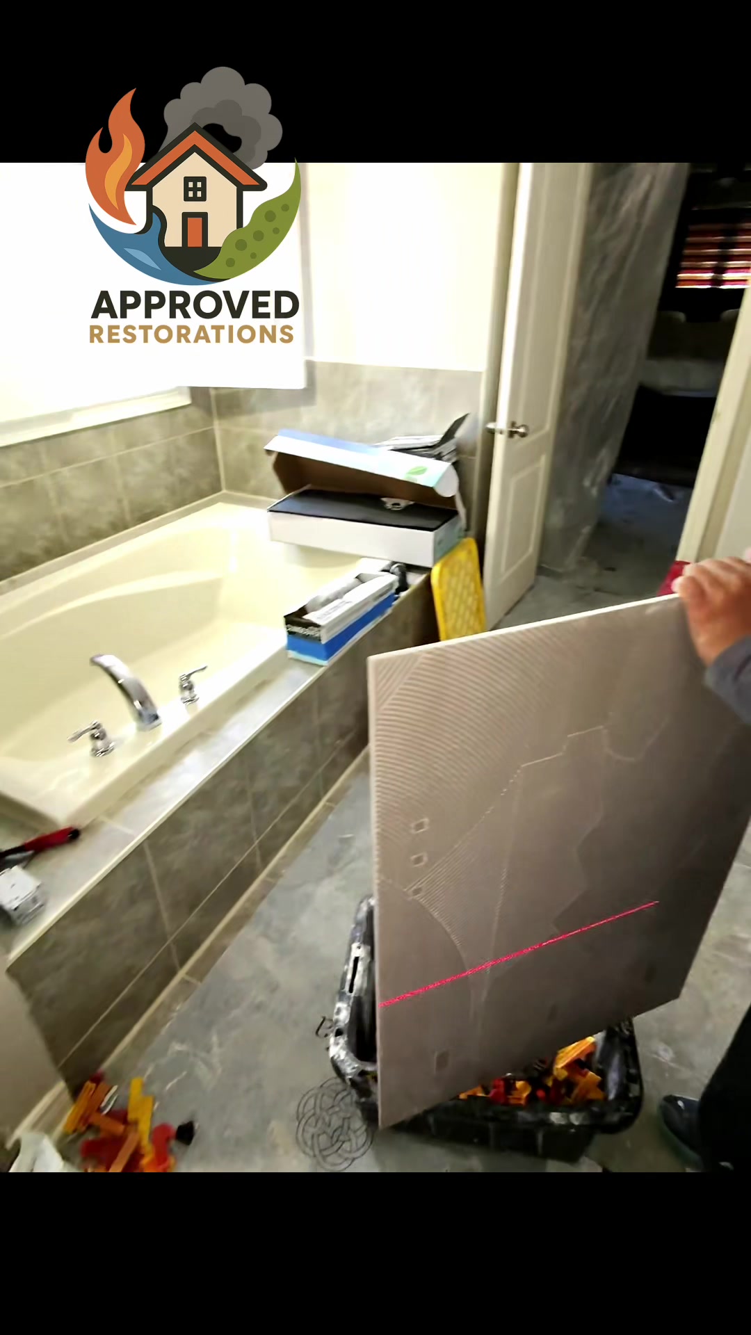 A persistent shower leak destroyed this bathroom floor and the ceiling below, so after tearing out the soaked subfloor and hanging plastic to protect the hallway, our crew is deep into the reconstruction phase, lining up a red laser level to precisely set large-format tiles and close out the insurance claim.