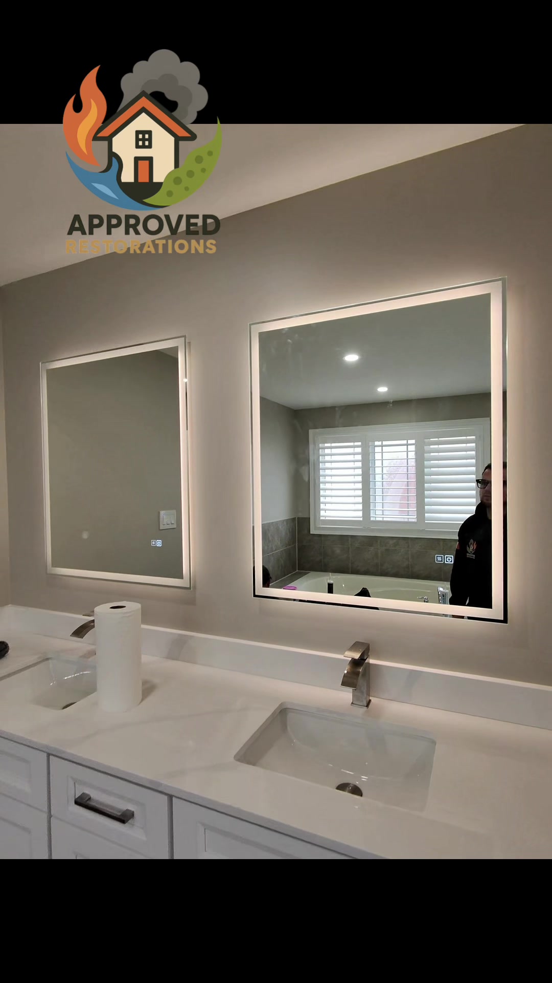 A persistent shower leak quietly saturated the bathroom floor and wrecked the ceiling downstairs, so our tech is inspecting this seemingly pristine space—catching his reflection in the illuminated vanity mirrors—to pinpoint the exact point of failure before we start tearing out the ruined drywall and mapping the full insurance claim.
