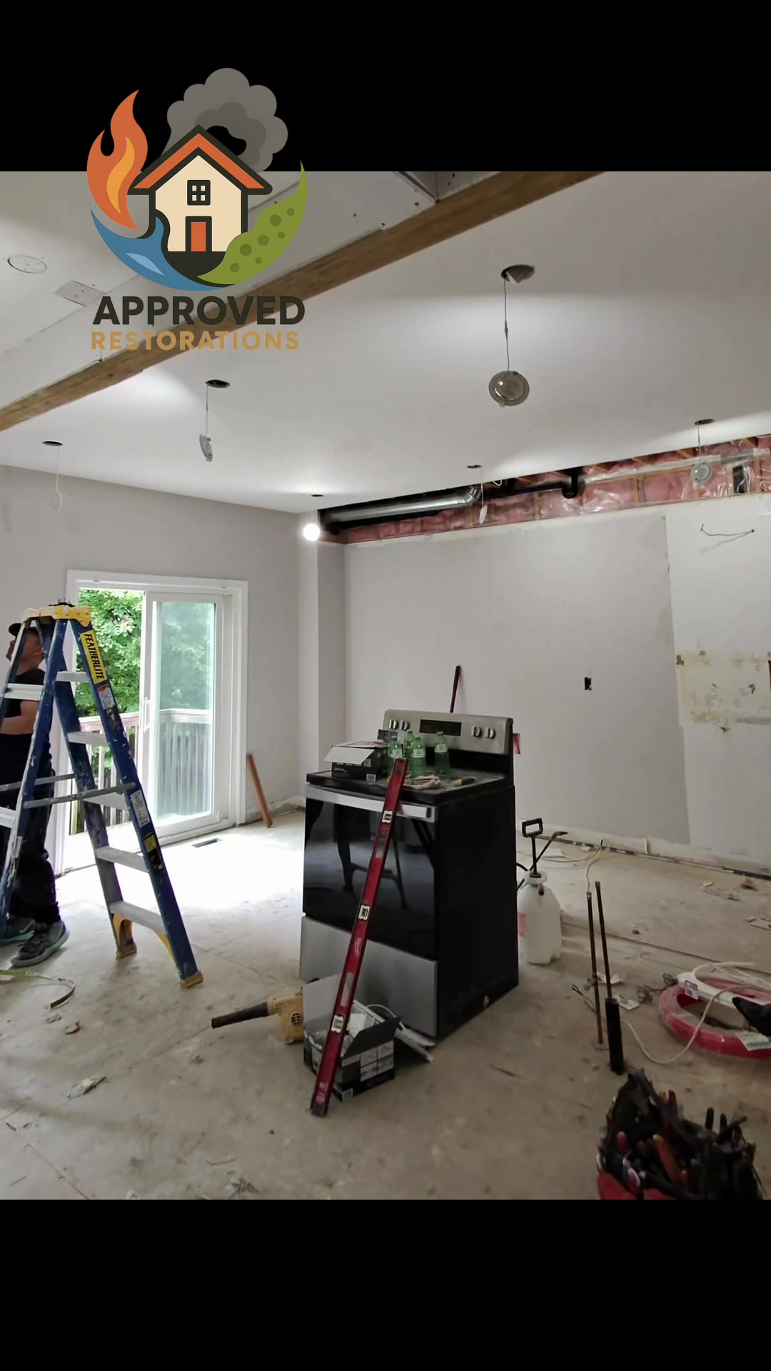Following a massive overhead leak that gutted this kitchen down to the bare concrete slab, our crew is deep into the reconstruction phase, working off ladders to secure hanging recessed lights and close up the exposed plumbing bulkhead before we can finally lay fresh flooring and slide the appliances back into place.