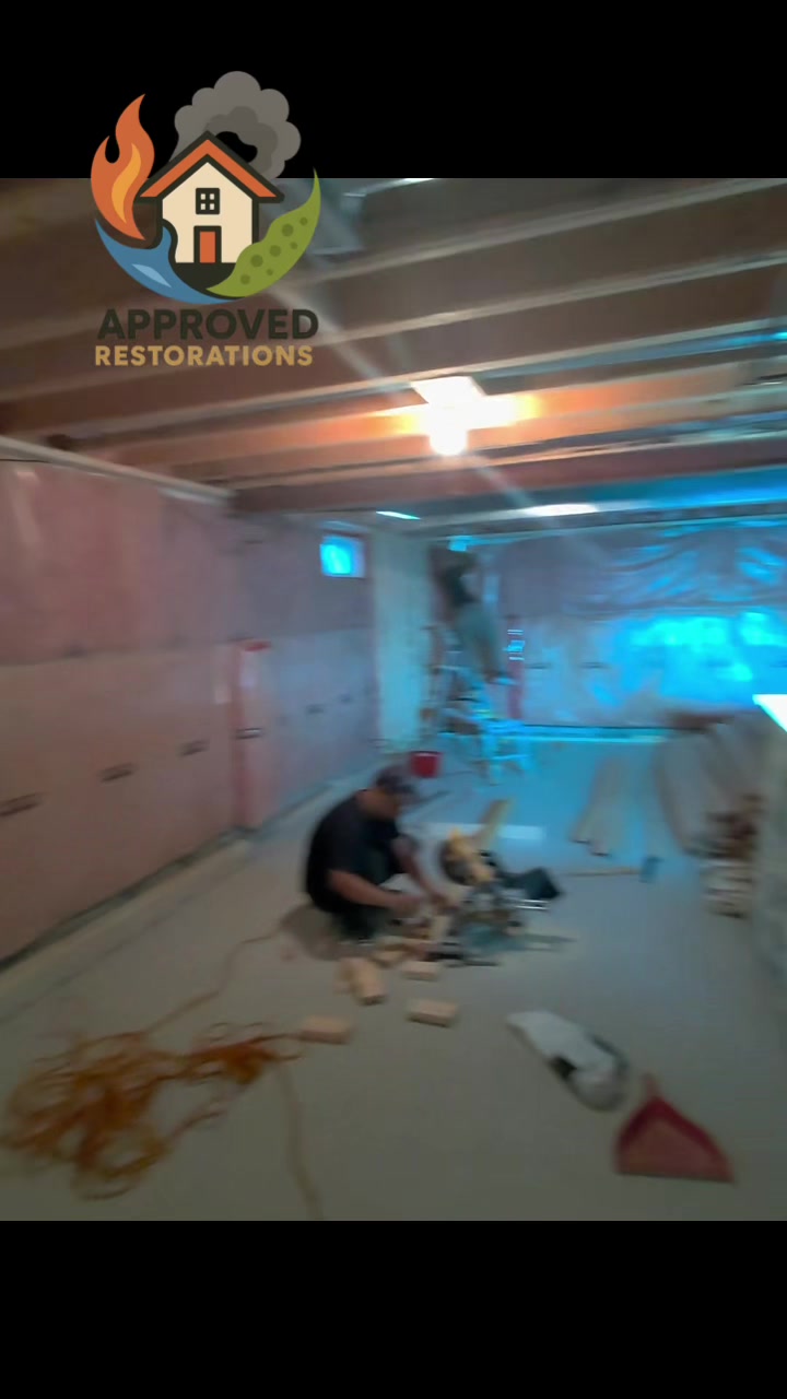 Deep into the reconstruction phase of a major water damage claim at this Vaughan home, our crew is running a miter saw on the bare concrete to cut fresh framing and prepping the back wall behind poly sheeting—we've already packed the studs with fresh pink insulation and are getting everything squared away to hang the new drywall.